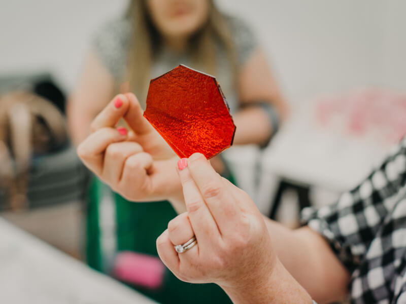 Close up of hands holding a piece of red glass in a glass craft class demonstration.